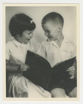 Studio portrait of a young girl and boy giggling over a shared book