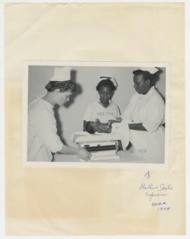 Three nurses weigh an infant